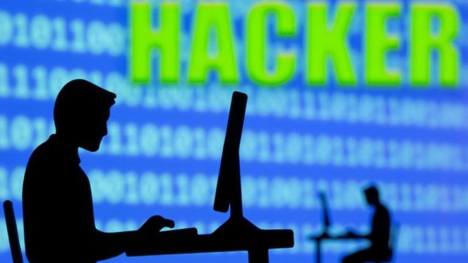 Minh họa người dùng ngồi trước máy tính với những dòng mã nhị phân và chữ hacker phía sau. Ảnh: Reuters