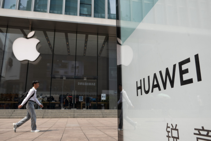 Một người đi ngang Apple Store ở Thượng Hải, phía trước là biển quảng cáo Huawei. Ảnh: Reuters